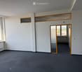 Empty room with grey carpet, white walls, large windows, and a glass door leading to another space.