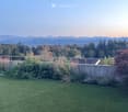 Well-maintained lawn with a metal railing, surrounded by trees and shrubs, with a scenic mountain view in the background.