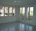 Empty room with tiled floor, large windows, and sliding glass doors leading to an outdoor area.