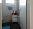 Modern bathroom with dark tiled floor, white walls, a window, a shower with a curtain, a towel rack with a blue towel, a small storage cabinet, and a toilet.