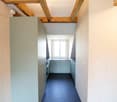 Modern hallway with exposed wooden beams, grey cabinets, and a blue carpeted floor leading to a windowed area.