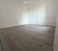 Empty room with light-colored walls and a wooden floor, featuring a single hanging light fixture.