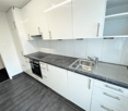 Modern kitchen with white cabinets, black countertops, stainless steel sink, and built-in oven.