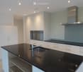 Modern kitchen with white cabinets, black countertops, stainless steel sink and faucet, built-in oven, and range hood.