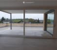 Empty room with tiled floor and large sliding glass doors opening to a tiled balcony with a view of the countryside.