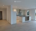 Modern kitchen with white cabinets, a central island, and a black countertop. Features include a range hood, sink, and large windows providing natural light.