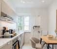 Modern kitchen with white cabinets, marble countertops, and stainless steel appliances. Features a breakfast area with a wooden table, two chairs, and a bowl of fruit on the table.