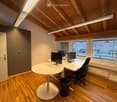 Modern office space with wooden flooring, white desk, round table, office chair, multiple computer monitors, and a trash can.