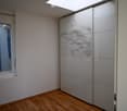 Empty room with wooden flooring, white walls, a large window with a perforated glass panel, and a sliding closet with mirrored doors.