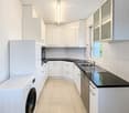 Modern kitchen with white cabinets, black countertops, a stainless steel sink, and a built-in washing machine.