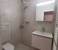 Modern bathroom with marble tiles, a toilet, a sink with a mirror, and a showerhead.