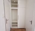 Empty hallway with white walls, wooden floor, and a built-in white closet with open shelves and drawers.