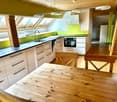 Modern kitchen with white cabinets, dark countertops, a wooden dining table, and two wooden chairs. Features a sink, faucet, and built-in oven.