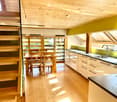 Bright, modern kitchen with wooden floors, white cabinets, and a dining area with a wooden table and chairs. Features large windows and skylights for natural light.
