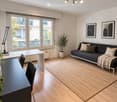 Modern living room with a dark grey sofa, a black coffee table, a white side table, a floor lamp, a woven rug, and potted plants.