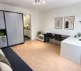 Modern, well-lit room with a sofa, desk, and cabinet. Features a kitchen area in the background with white cabinets and a countertop.