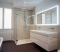 Modern bathroom with a bathtub, glass-enclosed shower, double sink with modern faucet, illuminated mirror, and a radiator.