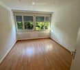 Empty room with wooden flooring, white walls, large windows with blinds, and radiators on the walls.