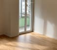 Empty room with light wooden flooring and large sliding glass doors leading to a balcony area.