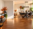 Modern dining area with wooden flooring, a sleek dining table surrounded by chairs, decorative vases, candles, and a small cart with additional decor.