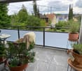 Balcony with tiled floor, metal railing, potted plants, small table, and a blanket draped over a chair.