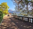 Pedestrian path surrounded by trees, leading to a lake with mountains in the background.