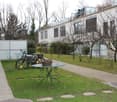 Garden area with a green lawn, a metal table, chairs, bicycles, and potted plants near a modern building with a balcony.