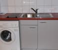 Compact kitchen with a sink, faucet, induction cooktop, and a washing machine tucked under the cabinets.