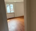 Empty room with wooden flooring, white walls, and a window with white frame and radiator below it.