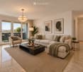 Modern living room with large windows, beige sofa, coffee table, armchair, floor lamp, side table, and decorative items.