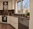 Modern kitchen with white cabinets, dark countertops, stainless steel appliances, and a large window overlooking a cityscape.