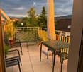 Balcony with tiled floor, green metal table and chairs, bench, umbrella, and potted plants.