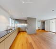 Modern kitchen with light-colored cabinets, a stainless steel sink, and wooden flooring. Large windows and sliding glass doors lead to an outdoor area.