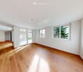 Empty room with wooden flooring, white walls, large windows, and sliding glass doors leading to an outdoor area.