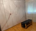 A clean, unfurnished room with wooden flooring, a massage table, and a large window with curtains.