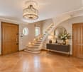 Elegant hallway with a staircase, chandelier, wooden doors, and a console table with a vase and books.