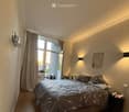 Modern bedroom with a large bed, nightstand, and a window with curtains leading to a balcony.