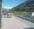 Balcony with a table and chairs, overlooking a scenic mountain landscape and green fields.