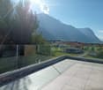 A modern balcony with a glass railing, tiled floor, and scenic mountain view.