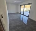 Empty room with dark grey tiled floor, white walls, and large sliding glass door leading to a balcony.