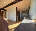 Open-plan living and kitchen area with wooden floors, exposed wooden beams, modern kitchen cabinets, and stainless steel appliances.