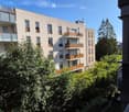 Modern multi-story residential building with balconies, large windows, and surrounding greenery.