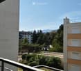 Balcony overlooking a residential area with trees, buildings, and distant mountains under a clear blue sky.