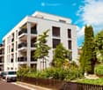 Modern multi-story residential building with white facade, balconies, and surrounding greenery.