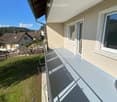 Balcony with a smooth grey surface, white-framed windows, and a view of a grassy yard and neighboring houses.