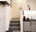 Modern hallway with white walls, grey carpet, black bench, grey steps leading up, white cabinets, sink, and vase with flowers.