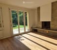 Bright living room with wooden flooring, large sliding glass doors leading to a garden, and a stone fireplace with a built-in bench.