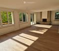 Empty room with wooden flooring, large windows, and a fireplace area. No furniture or equipment present.