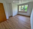 Empty room with wooden flooring, white walls, large window with wooden sill, white built-in closet, and a radiator below the window.