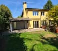 Two-story yellow house with a chimney, garage, and well-maintained garden.